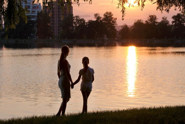 Happy mom and daughter girl relaxing holding hands enjoying time together in summer park at sunset Family love and relationship concept