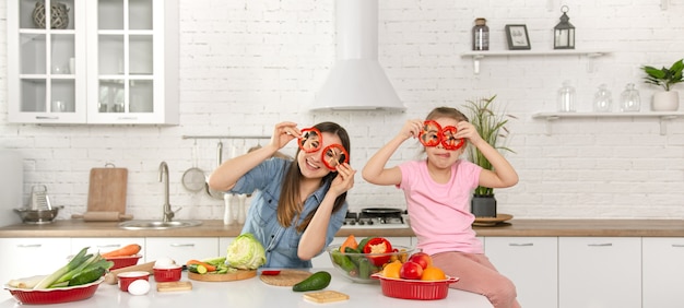 Happy mom and daughter posing with pepper rings while cooking salad.