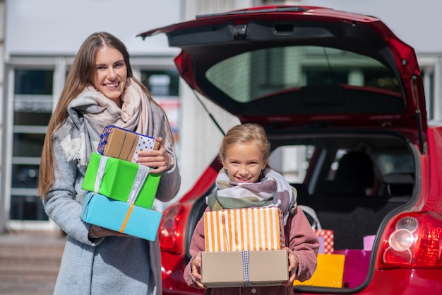 Felice mamma e figlia in piedi con scatole regalo nel bagagliaio dell'auto