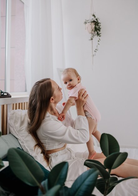 Happy mom is playing with a baby baby on the bed in the room