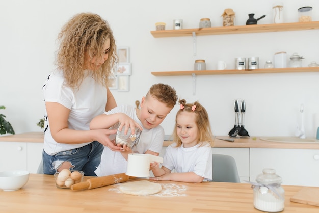 Happy mom and kids mixing ingredients for homemade cake, pie or cookie dough in the kitchen.