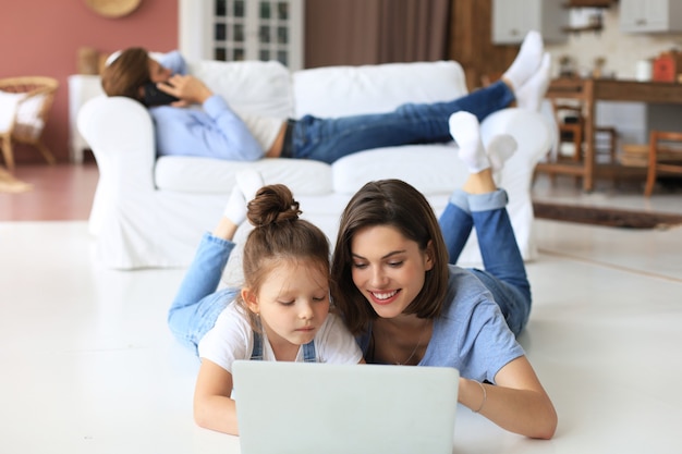 행복한 엄마와 어린 소녀는 화면 노트북을 보고, 웹캠과 대화하고, 컴퓨터 앱을 통해 온라인 채팅을 합니다.