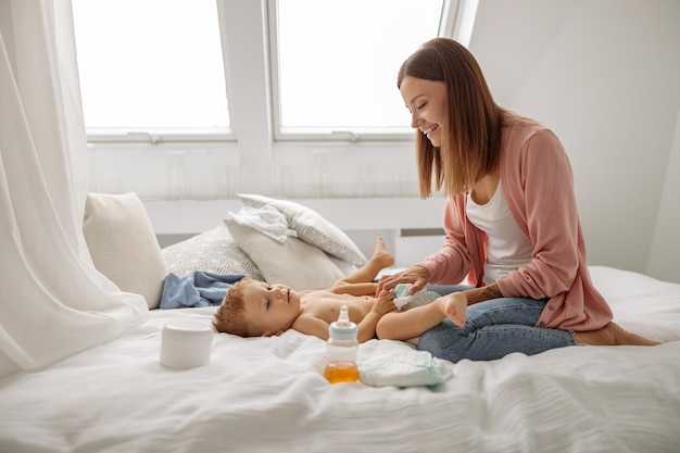 Happy mom putting diaper on her baby in nursery