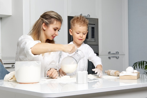Mamma e figlio felici si divertono a cucinare in una cucina bianca a tavola