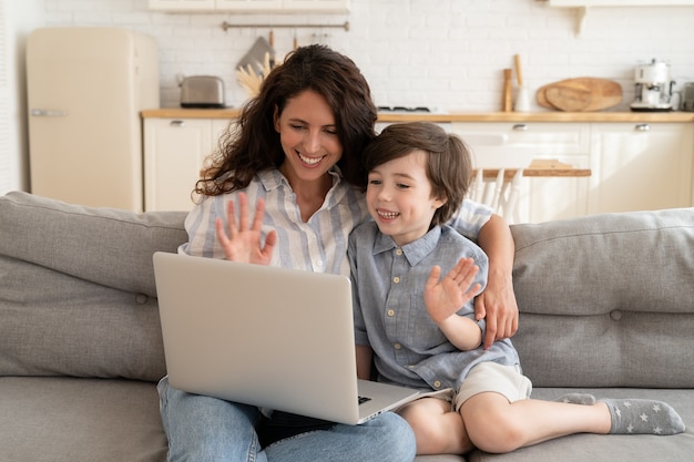 Happy mom and son use video connection to call to grandparents or dad on business trip wave hands