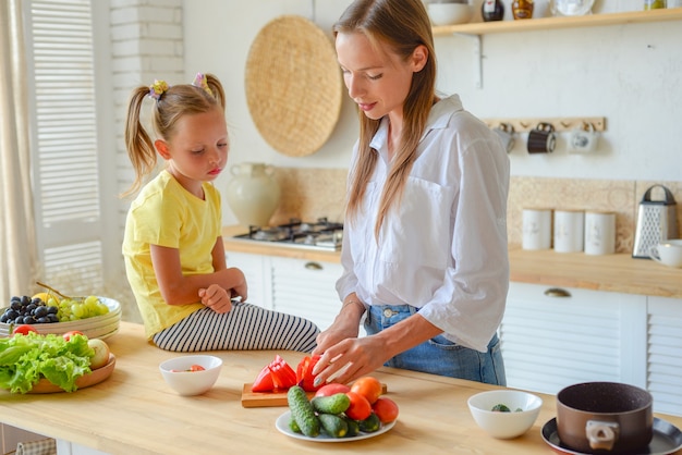 Happy mom teaches little daughter to cook healthy food mom and girl talking smiling