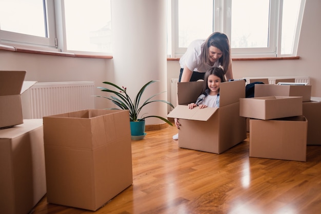 Photo happy mom with daughter or child are moving in the house and having fun unpacking all in boxes