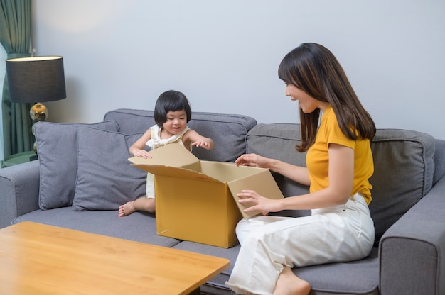 A happy mom with daughter opening cardboard box in living room at home