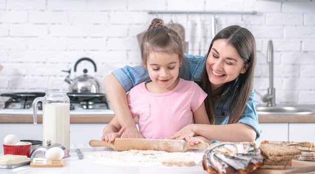 Happy mom with daughter preparing homemade cakes in a light kitchen close up.