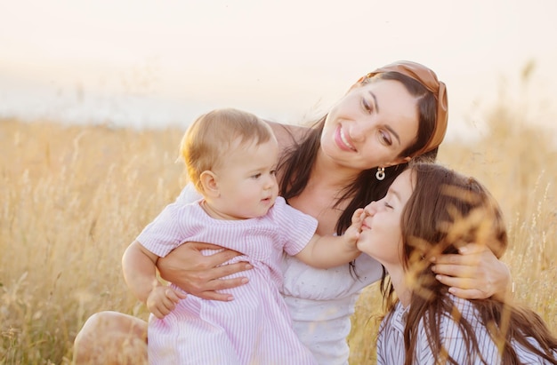 Happy mom with two little daughters on summer field at sunset