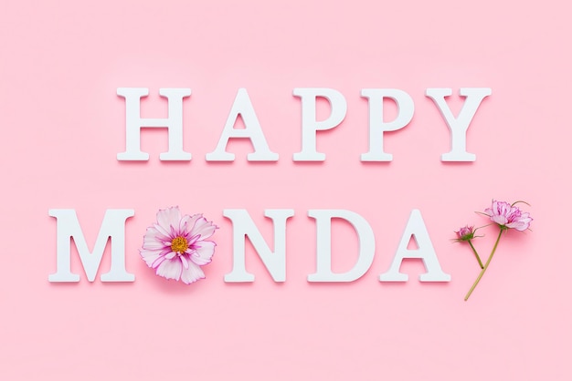 Happy Monday Motivational quote from white letters and beauty natural flowers on pink background Creative concept Hello Monday positive mood