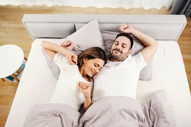 Happy morning couple waking up and stretching in their bed at the comfortable home