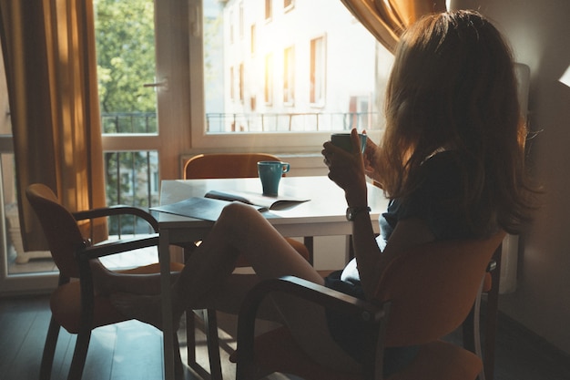 Buongiorno - la ragazza è seduta in cucina e beve il caffè mattutino