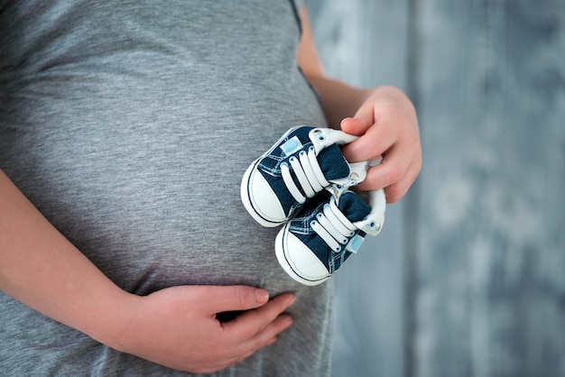 Happy mother in anticipation of the birth of her son Pregnant woman holding baby booties 