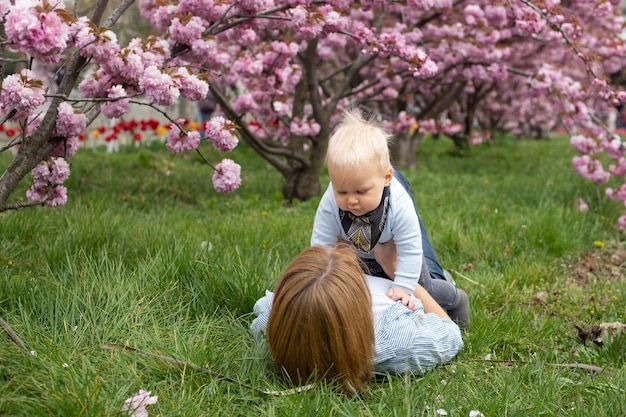 Happy mother in a blue shirt playing with a baby son in spring Motherhood and femininity