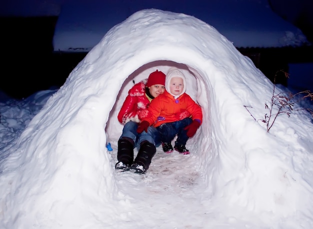 Foto felice madre e bambino seduti nel castello di neve al crepuscolo