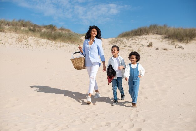 Felice madre e bambini che camminano sulla spiaggia. famiglia afroamericana che trascorre del tempo insieme all'aria aperta. tempo libero, tempo in famiglia, concetto di genitorialità