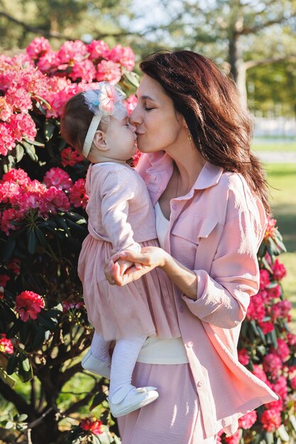 Happy mother and daughter are enjoying time in a stunning park next to flowering bushes