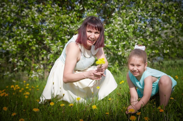 Happy mother and daughter enjoying rest playing and fun on nature on a green lawn with dandelions