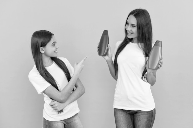 Photo happy mother and daughter hold shampoo bottle on blue background point finger