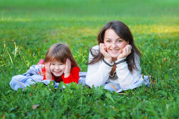 Happy mother and daughter lie on the grass in the park