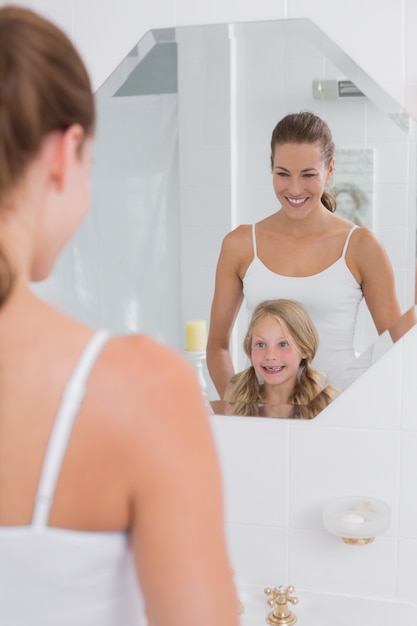 Happy mother and daughter looking at bathroom mirror