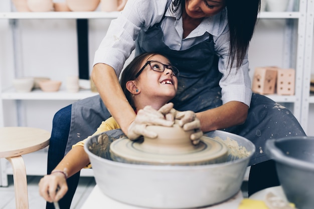 Happy mother and daughter making clay pottery on a spin wheel.