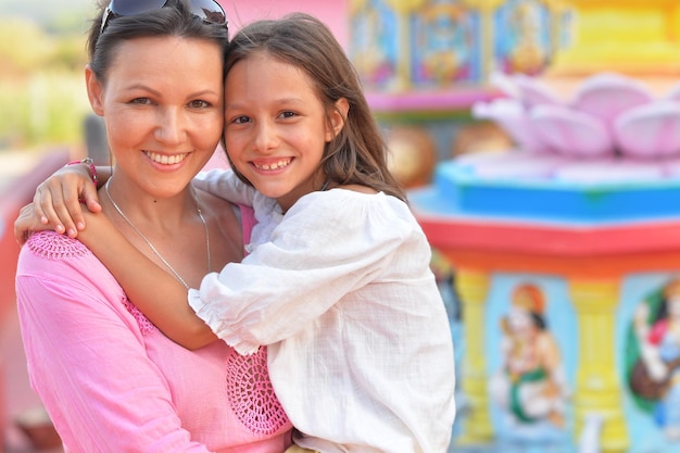 Happy mother and daughter posing on blurred amusement park background