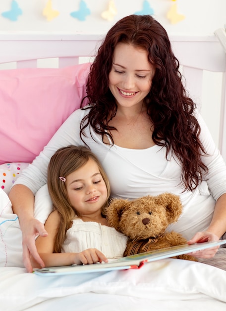 Happy mother and daughter reading in bed