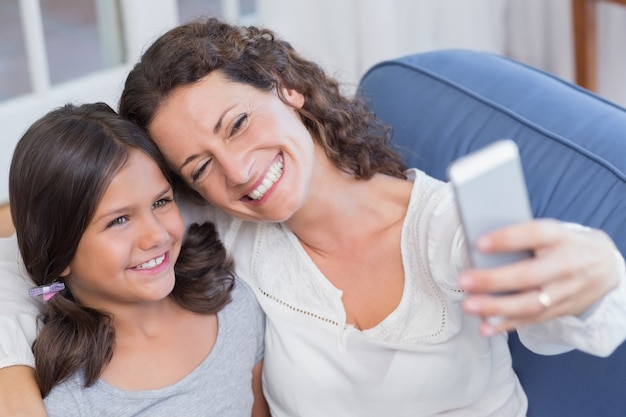 Happy mother and daughter sitting on the couch and taking selfie