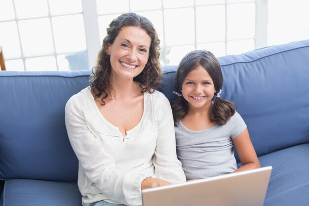 Happy mother and daughter sitting on the couch and using laptop