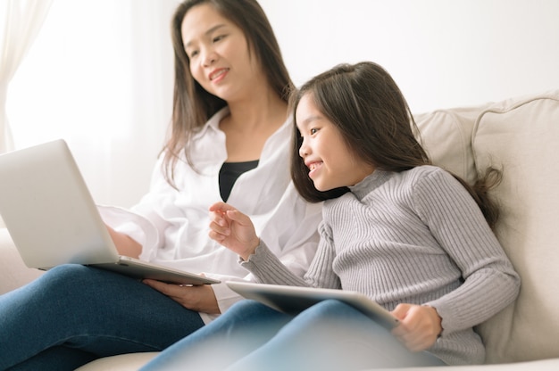 Madre e figlia felici con il pc della compressa e del computer portatile