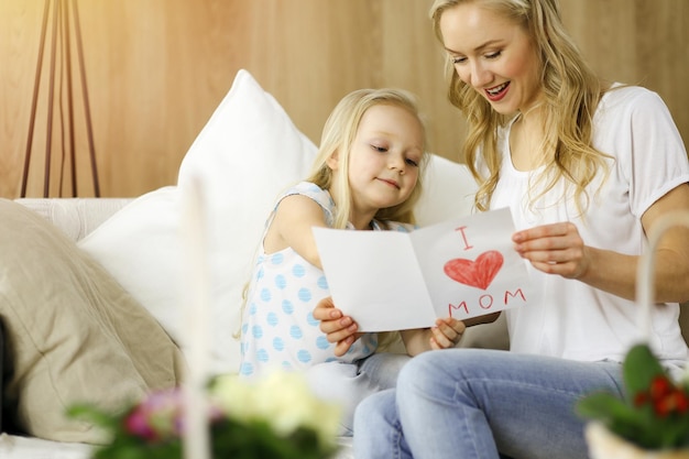 Happy mother day in sunny flat. child daughter congratulates\
mom and gives her postcard with heart drawing. family concept.