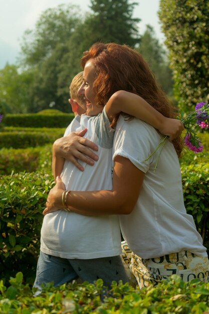 Photo happy mother embracing son while standing amidst plants in park