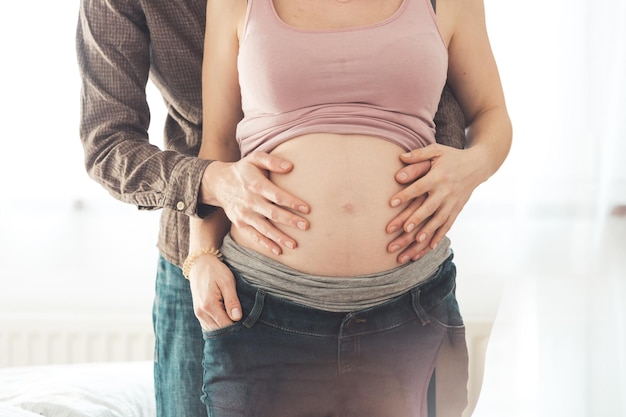 Счастливая мать и отец обнимают беременный живот крупным планом