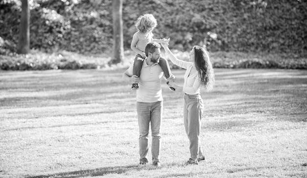 Happy mother and father carrying boy child on shoulders summer outdoors family leisure