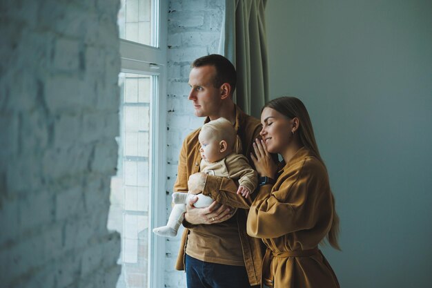 A happy mother and father hold their 4monthold son in their arms and look out the window of their apartment Homemade family photo of happy parents with a newborn baby Family concept