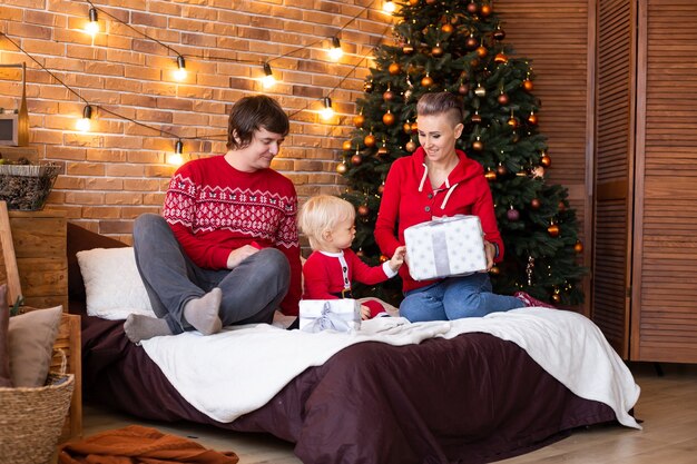 Happy mother, father and little child having fun near Christmas tree at home on bed. Enjoying time together on holidays.