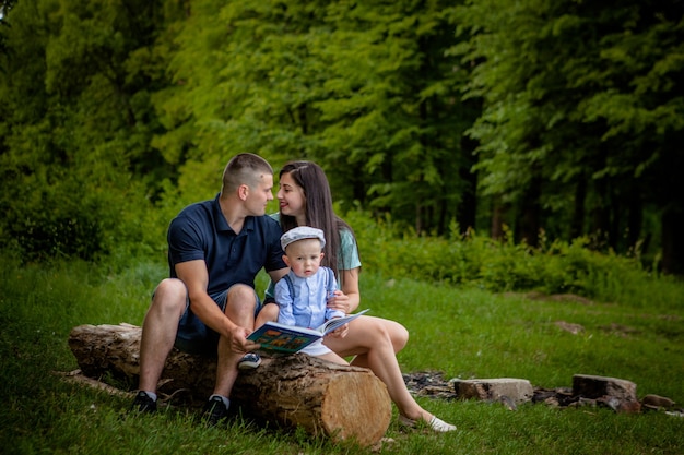 Happy mother, father and son read a book in the park.