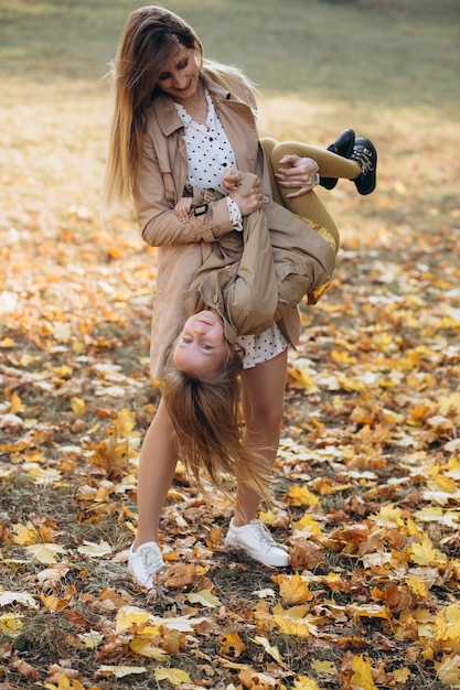 幸せな母と彼女の美しい娘は楽しんで、秋の公園を散歩します。