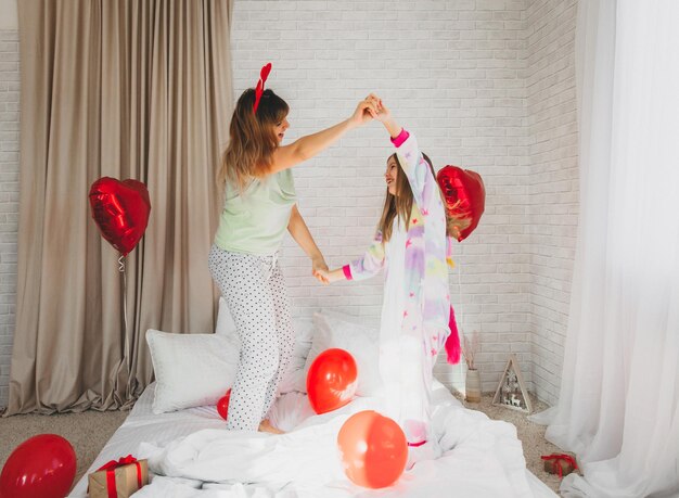 Happy mother and her daughter are jumping on the bed in the bedroom decorated for valentine's day.