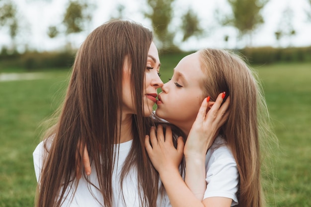 Photo a happy mother and her daughter are sitting on the grass in the park and hugging mother and daughter familyjoyful mom and little girl