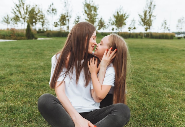 Photo a happy mother and her daughter are sitting on the grass in the park and hugging mother and daughter familyjoyful mom and little girl