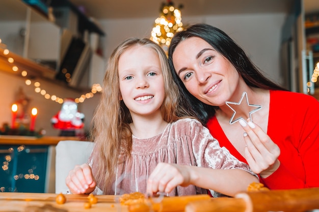 Happy mother and her daughter cooking Christmas cookies at kitchen