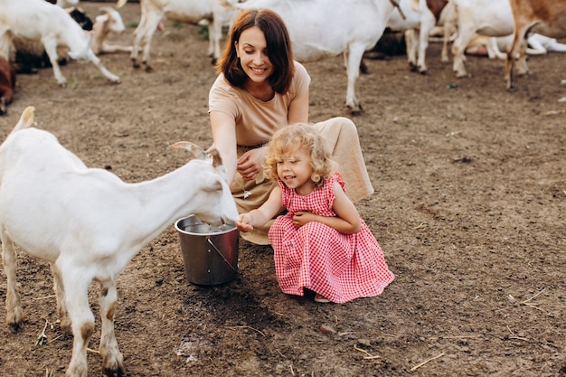 Happy mother and her daughter spend time on an eco farm among goats.