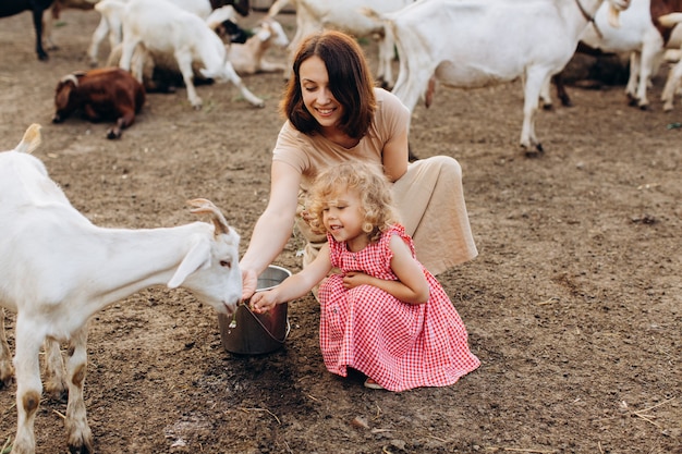 Happy mother and her daughter spend time on an eco farm among goats.