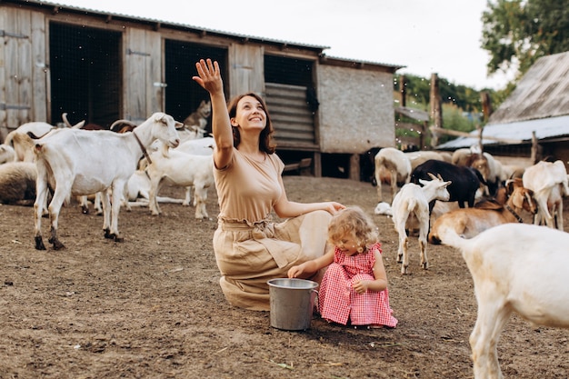 Happy mother and her daughter spend time on an eco farm among goats.