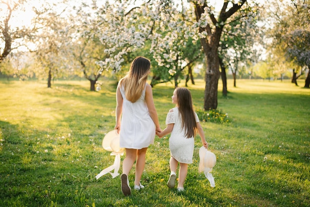 Happy mother and her daughter in white dresses run through the spring garden at sunset