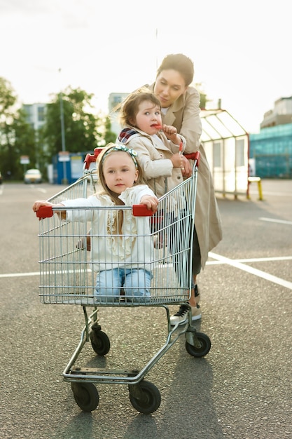 La madre felice e le sue figlie si divertono con un carrello della spesa