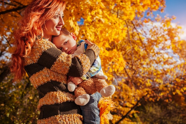 Happy mother and her little son walking in autumn forest Woman holding her child